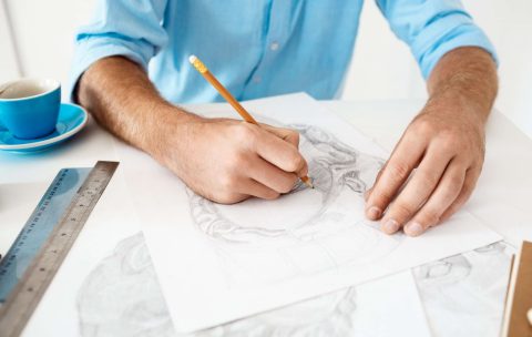 hands-young-businessman-sitting-table-with-pencil-drawing-portrait-white-modern-office-interior-min-scaled